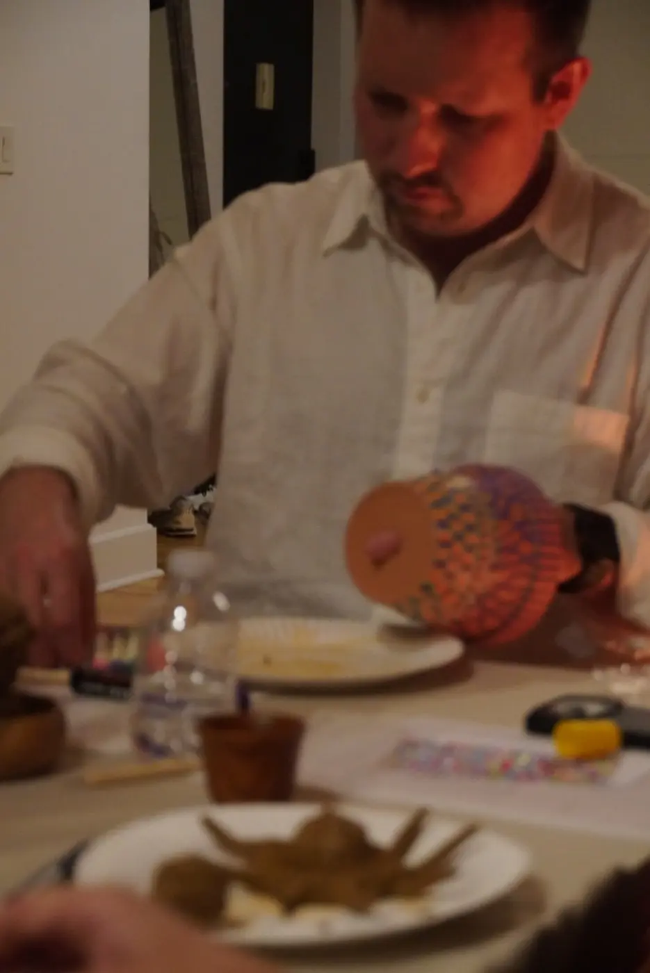 a guest in a white shirt holding up a terracotta pot painted in orange, purple and green dots, during an art therapy night in a SoHo living room, New York