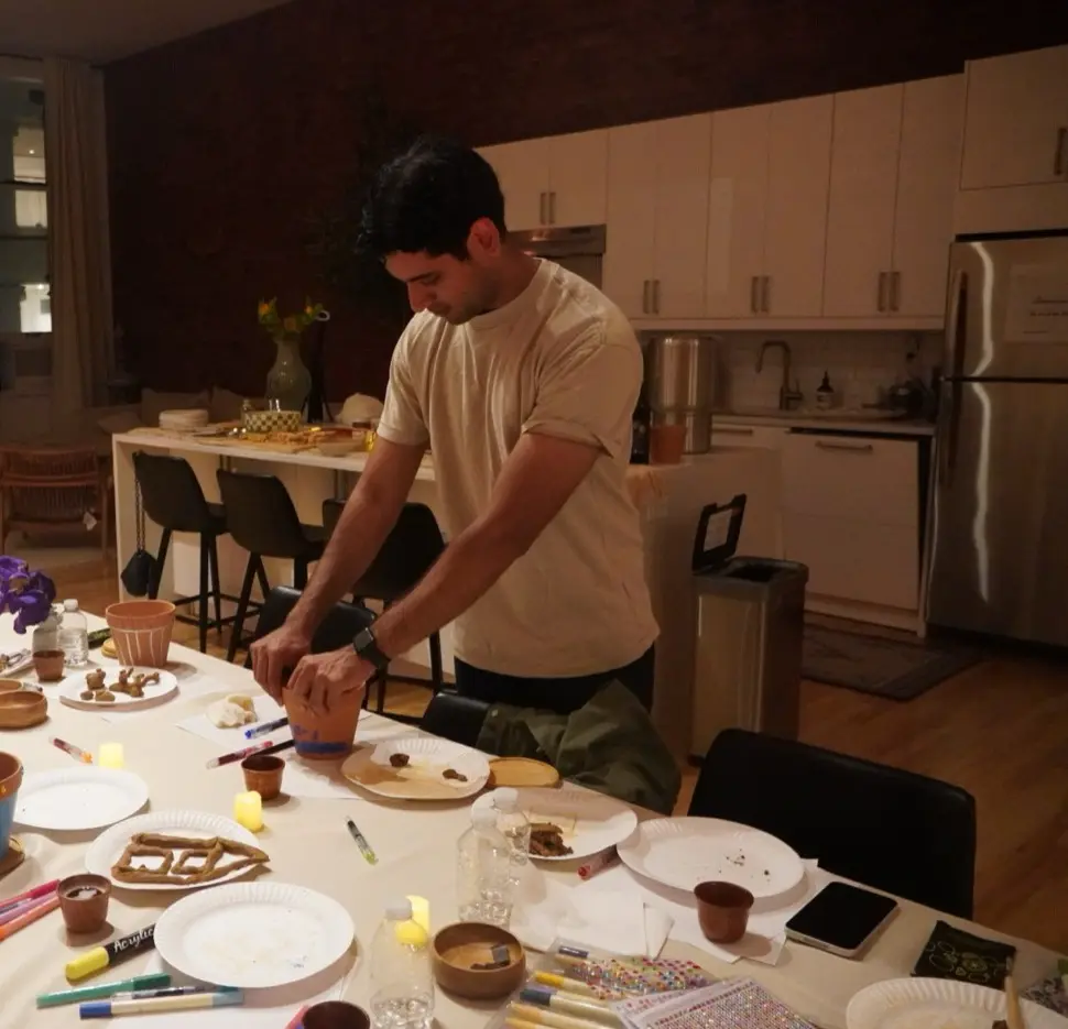 a guest standing at the long table shaping a painted pot, with the kitchen behind, during an art therapy night in a SoHo living room, New York