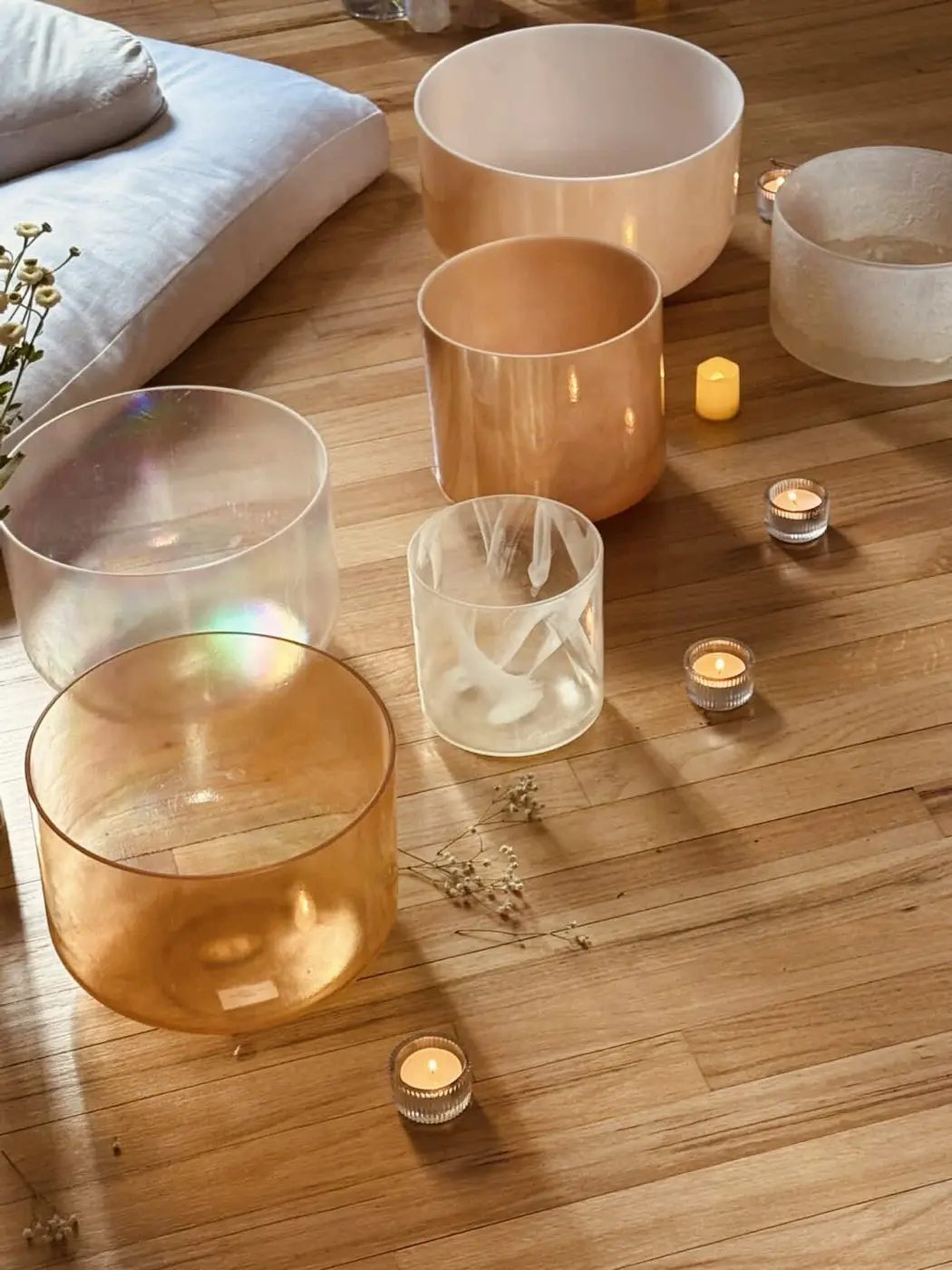 amber and clear crystal bowls on a wooden floor beside tealights, dried flowers and a linen cushion, set up for a sound bath in a SoHo living room, New York