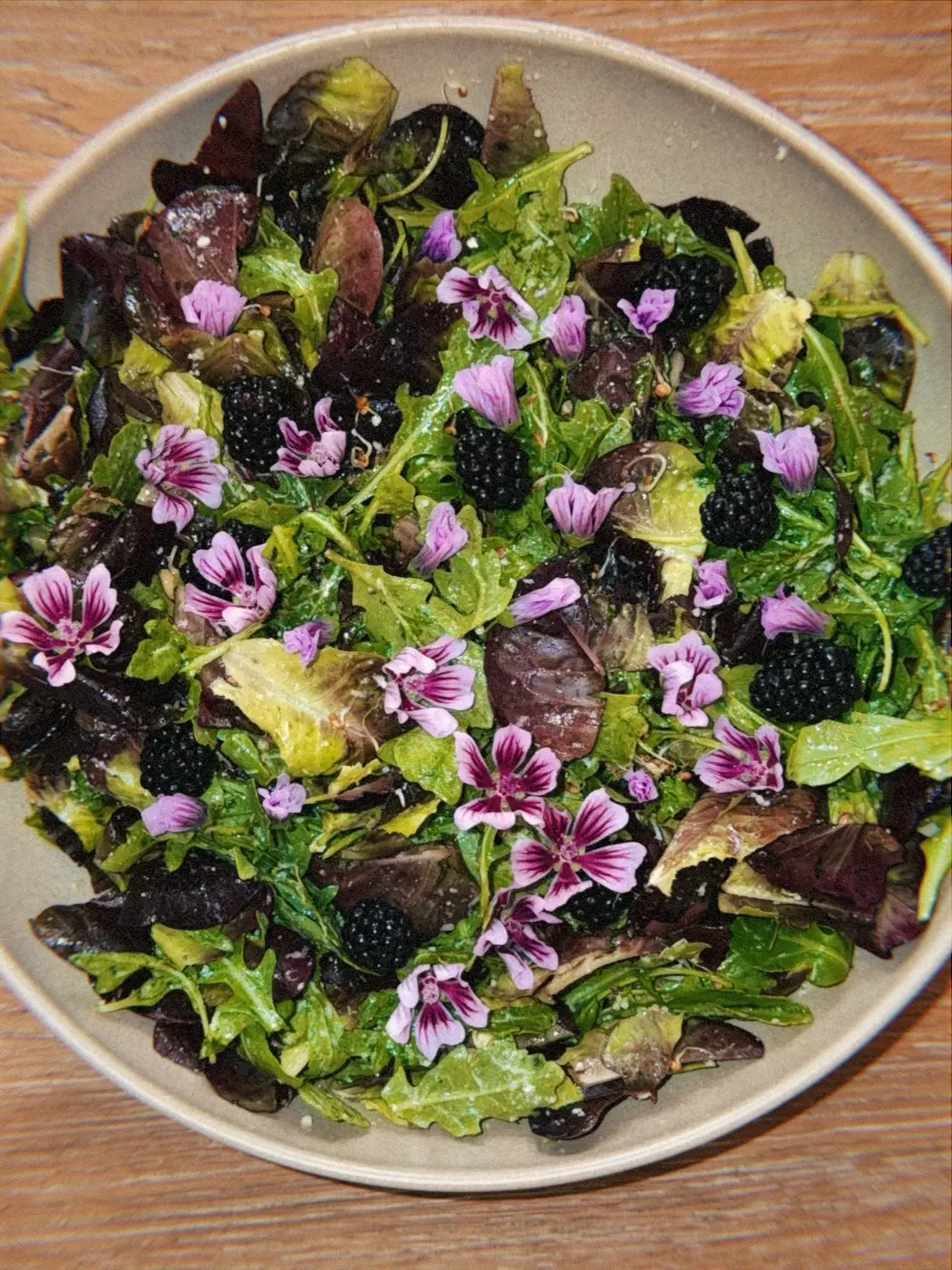 a wide bowl of leaves, blackberries and edible pink flowers on a wooden table, at a sound bath gathering in a SoHo living room, New York