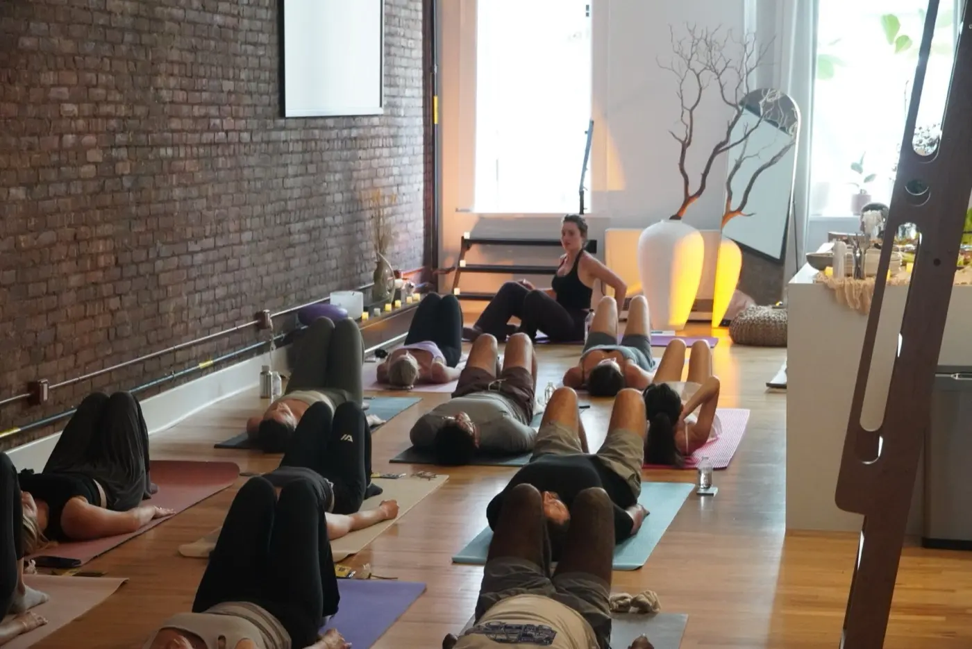 guests lying on mats with knees bent while a practitioner talks them through the sequence, during a pilates class in a SoHo living room, New York