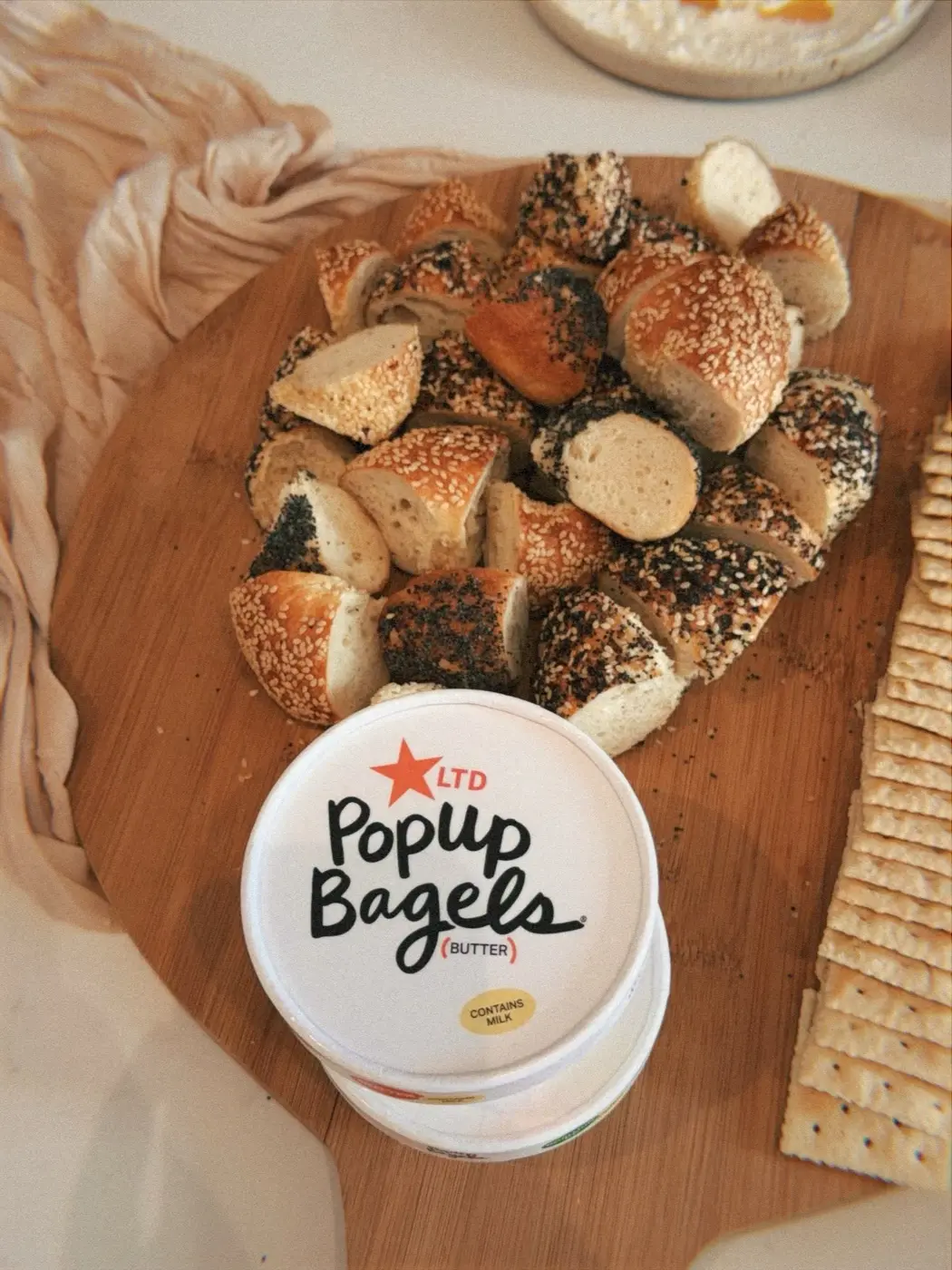 a wooden board of sliced sesame and poppy seed bagels beside a tub of cream cheese and crackers, at an art therapy night in a SoHo living room, New York